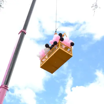 Picture of a man cage covered in pink and white balloons on the day of the Pink Lady crane launch