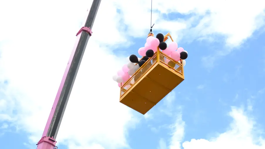 Picture of a man cage covered in pink and white balloons on the day of the Pink Lady crane launch